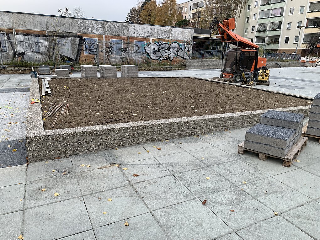 Bauarbeiter mit Bagger und Schubkarre bei der Arbeit auf einer Baustelle mit Betonplatten und Erde.