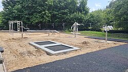 Sportfläche mit Sandboden, zwei eingebauten Trampolinen und mehreren Fitnessgeräten im Freien