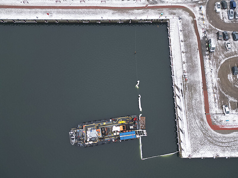 Luftaufnahme des Stadthafens mit einem Schiff im Wasser und schneebedecktem Ufer