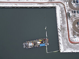 Luftaufnahme des Stadthafens mit einem Schiff im Wasser und schneebedecktem Ufer