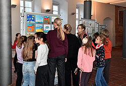 Gruppe von Kindern und einer erwachsenen Person in einem Raum mit bunten Bildern an der Wand