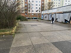Eine Person geht auf einem gepflasterten Weg neben einer hohen Mauer mit Graffiti mit Wohngebäuden im Hintergrund.