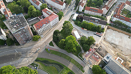 Luftaufnahme einer Baustelle neben einem historischen Rathaus, umgeben von Wohngebäuden und Straßen mit Straßenbahnschienen