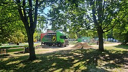 LKW mit Aufschrift "Kunststofffolien-Service" steht auf einem von Bäumen umgebenen Platz neben einem Erdhaufen