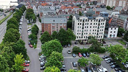 Blick auf eine von Bäumen gesäumte Straße mit parkenden Autos und Gebäuden.