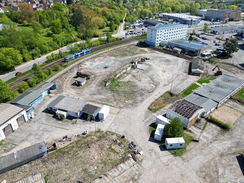 Luftaufnahme des großen, unbebauten Baugrundstücks mit einigen alten Gebäuden und Baumaschinen, umgeben von Grünflächen und dem nahegelegenen Wohngebiet Dierkow