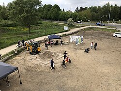 Blick von oben auf einen Sandkasten. Daneben einige Menschen.