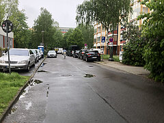 Putbuser Straße vor der Sanierung. Blick auf eine regennasse Straße mit parkenden Autos beidseitig. Bäume und Gebäude im Hintergrund sind sichtbar.