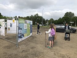 Personen schauen auf Bauzäune an denen etwas aufgehangen ist.