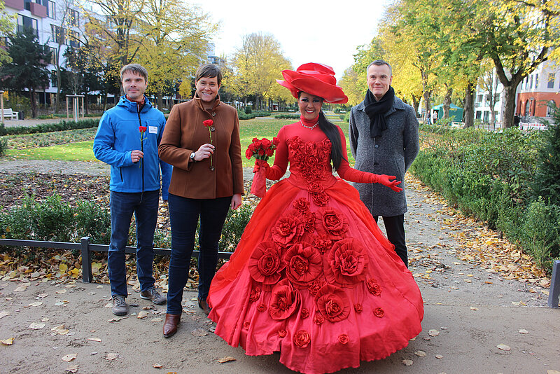Zwei Männer und zwei Frauen lächeln in die Kamera. Eine Frau trägt ein Rosenkostüm.