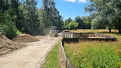 Baustelle mit einem Radlader auf einem unbefestigten Weg neben einer Wiese und Bäumen