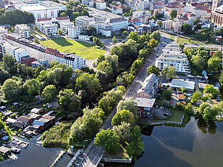 Blick auf Mühlendamm und Bleichergraben Luftaufnahme eines Flusses mit Brücke, umgeben von Bäumen und Wohngebäuden am Mühlendamm