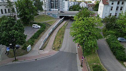 Blick auf eine Straßenunterführung mit Grünflächen, Bäumen und umliegenden Wohngebäuden