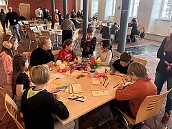 Menschen sitzen an einem langen Tisch in einem hellen Raum und unterhalten sich
