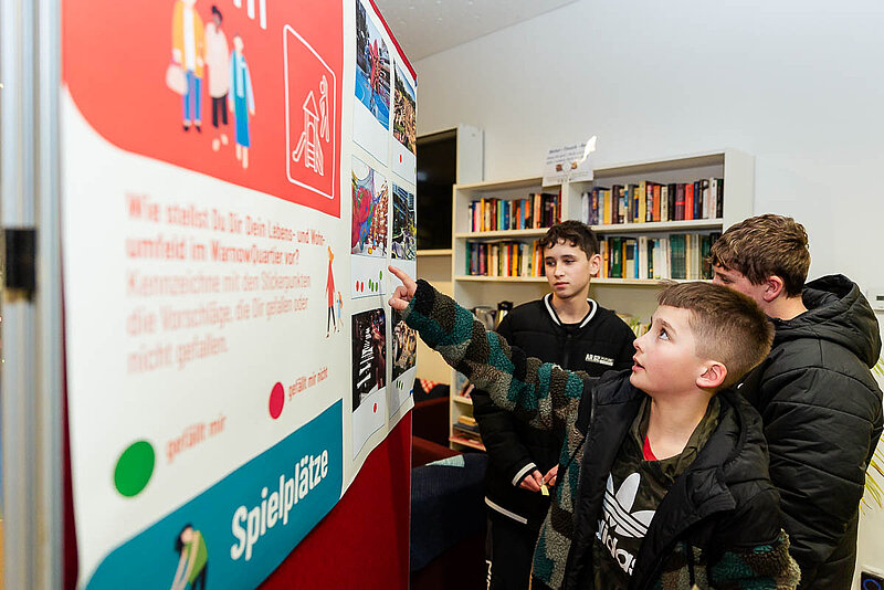 Drei Jungs stehen vor einer Stellwand und zeigen auf etwas.