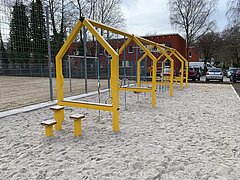 Gelbes Spielgerät mit Sportelementen auf einem Spielplatz.