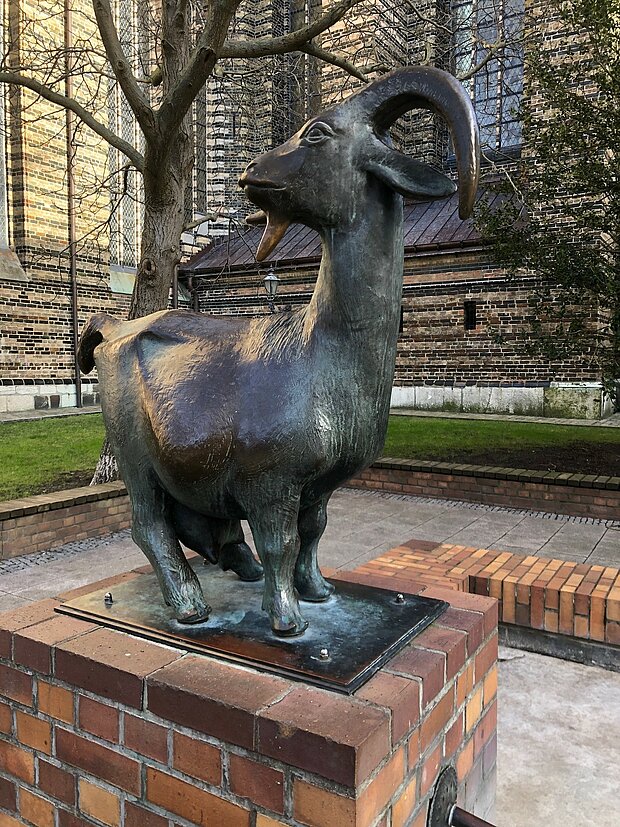 Eine Bronzestatue einer Ziege, die auf einem Ziegelblock steht und den sogenannten Ziegenbrunnen aus Stein ziert..