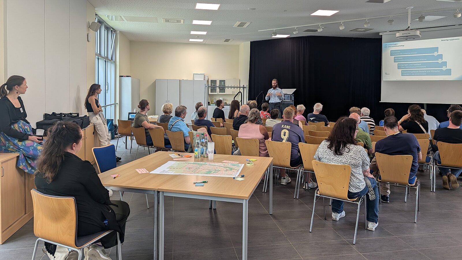 Blick in einem Raum mit vielen Menschen, die einer Präsentation zuhören.