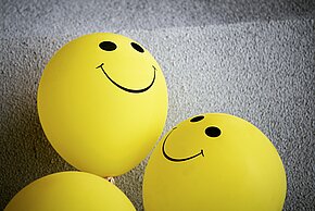 Zwei gelbe Smiley-Bälle mit lächelnden Gesichtern auf grauem Hintergrund.