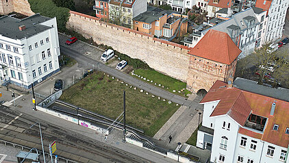 Luftaufnahme des Grundstücks mit der historischen Stadtmauer und den alten Gebäuden in Umgebung des Grundstücks. Im Vordergrund sind Straßenbahnschienen und Fahrzeuge sichtbar.