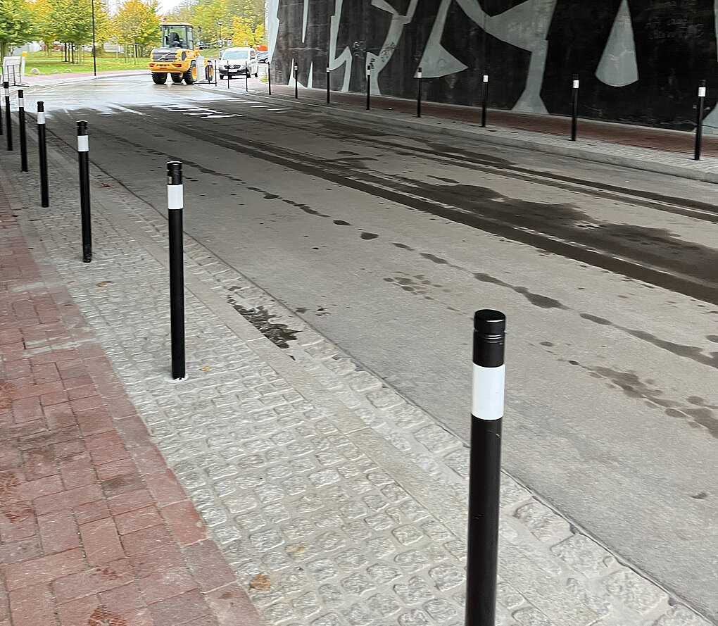 Straßendurchfahrt mit schwarzem Geländerpfosten mit weißen Streifen, nassem Asphalt und grauem Kopfsteinpflaster am Rand