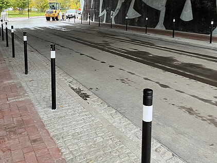 Straßendurchfahrt mit schwarzem Geländerpfosten mit weißen Streifen, nassem Asphalt und grauem Kopfsteinpflaster am Rand