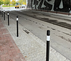 Straßendurchfahrt mit schwarzem Geländerpfosten mit weißen Streifen, nassem Asphalt und grauem Kopfsteinpflaster am Rand