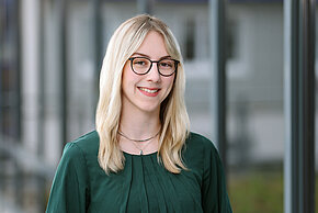 Frau mit blonden langen Haaren und Brille lächelt in die Kamera.