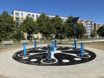 Outdoor-Spielgerät in einem Kreis auf einem Sandplatz, umgeben von Wohngebäuden und Bäumen
