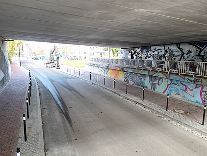 Straße unter einer Brücke mit  mehreren Pfosten entlang des Gehwegs