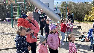 Kinder spielen und stehen in einer Reihe auf einem gepflasterten Spielplatz bei sonnigem Wetter