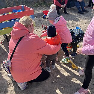 Kinder und Erwachsene spielen gemeinsam im Sandkasten, graben mit Schaufeln und Eimern