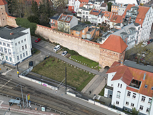 Luftaufnahme des Grundstücks mit der historischen Stadtmauer und den alten Gebäuden in Umgebung des Grundstücks. Im Vordergrund sind Straßenbahnschienen und Fahrzeuge sichtbar.