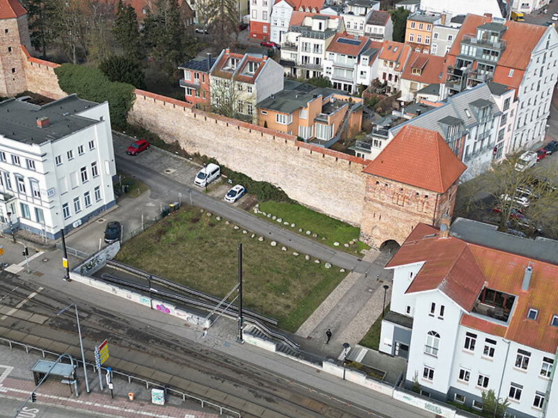 Luftaufnahme des Grundstücks mit der historischen Stadtmauer und den alten Gebäuden in Umgebung des Grundstücks. Im Vordergrund sind Straßenbahnschienen und Fahrzeuge sichtbar.
