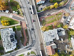 Luftaufnahme einer Brückenüberführung mit Straßenbahn, mehreren Fahrzeugen, Fußwegen und umgebenden Gebäuden