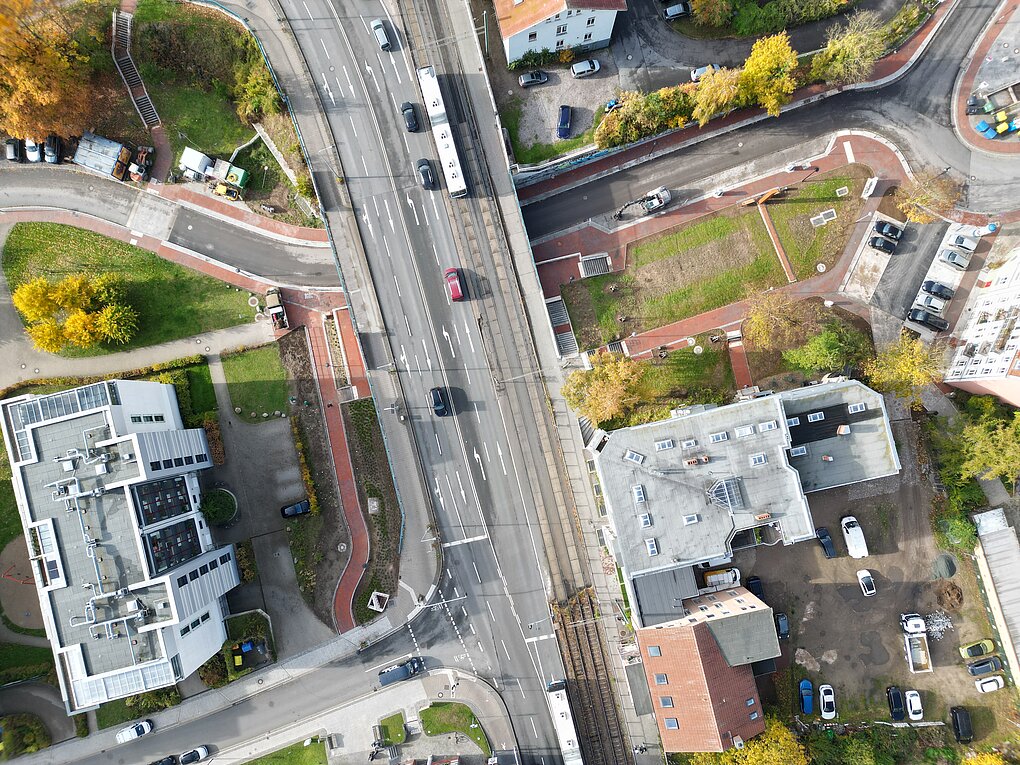 Luftaufnahme einer Brückenüberführung mit Straßenbahn, mehreren Fahrzeugen, Fußwegen und umgebenden Gebäuden