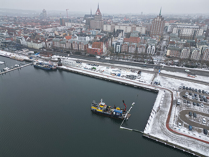 Luftaufnahme des verschneiten Stadthafens mit einem Schiff im Wasser und des Stadtzentrums im Hintergrund