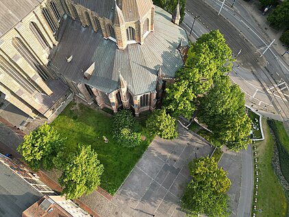 Luftaufnahme eines gepflasterten Platzes mit Bäumen und Schatten der Marienkirche.
