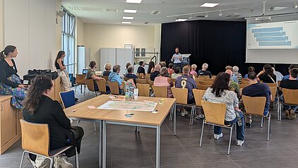 Blick in einem Raum mit vielen Menschen, die einer Präsentation zuhören.