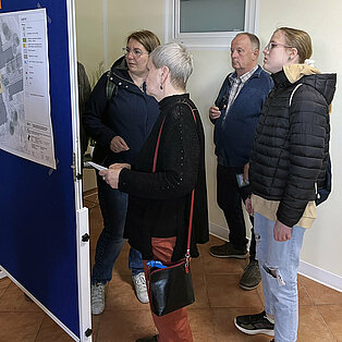 Gruppe von vier Personen die auf eine Stellwand schauen und diskutieren.