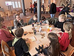 Gruppe von Menschen sitzt an einem großen Tisch und arbeitet gemeinsam an einem Projekt