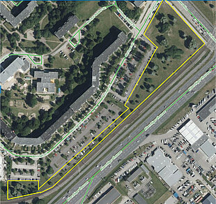 Luftaufnahme eines Wohngebiets mit Parkplätzen, angrenzender Straße und markiertem Bereich in Gelb