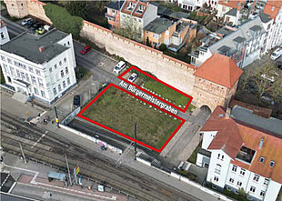 Luftaufnahme des unbebauten Grundstücks mit der Beschriftung 'Am Bürgermeistergraben'. Umgeben von Gebäuden und der Stadtmauer.