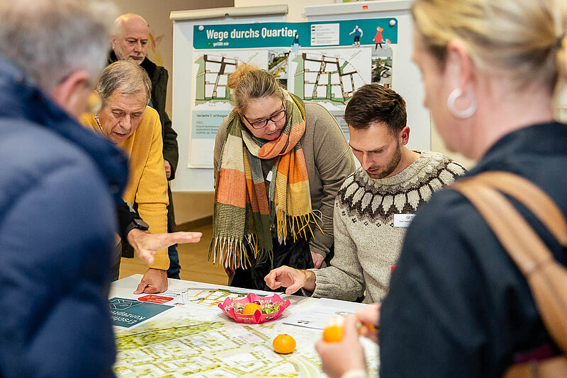 Menschen stehen um einen Tisch mit Karten und diskutieren und zeigen auf die Materialien