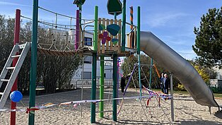 Bunter Spielplatz mit Klettergerüst, Rutsche und Hängebrücke auf Sandboden, abgesperrt mit Absperrband