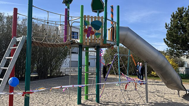 Bunter Spielplatz mit Klettergerüst, Rutsche und Hängebrücke auf Sandboden, abgesperrt mit Absperrband