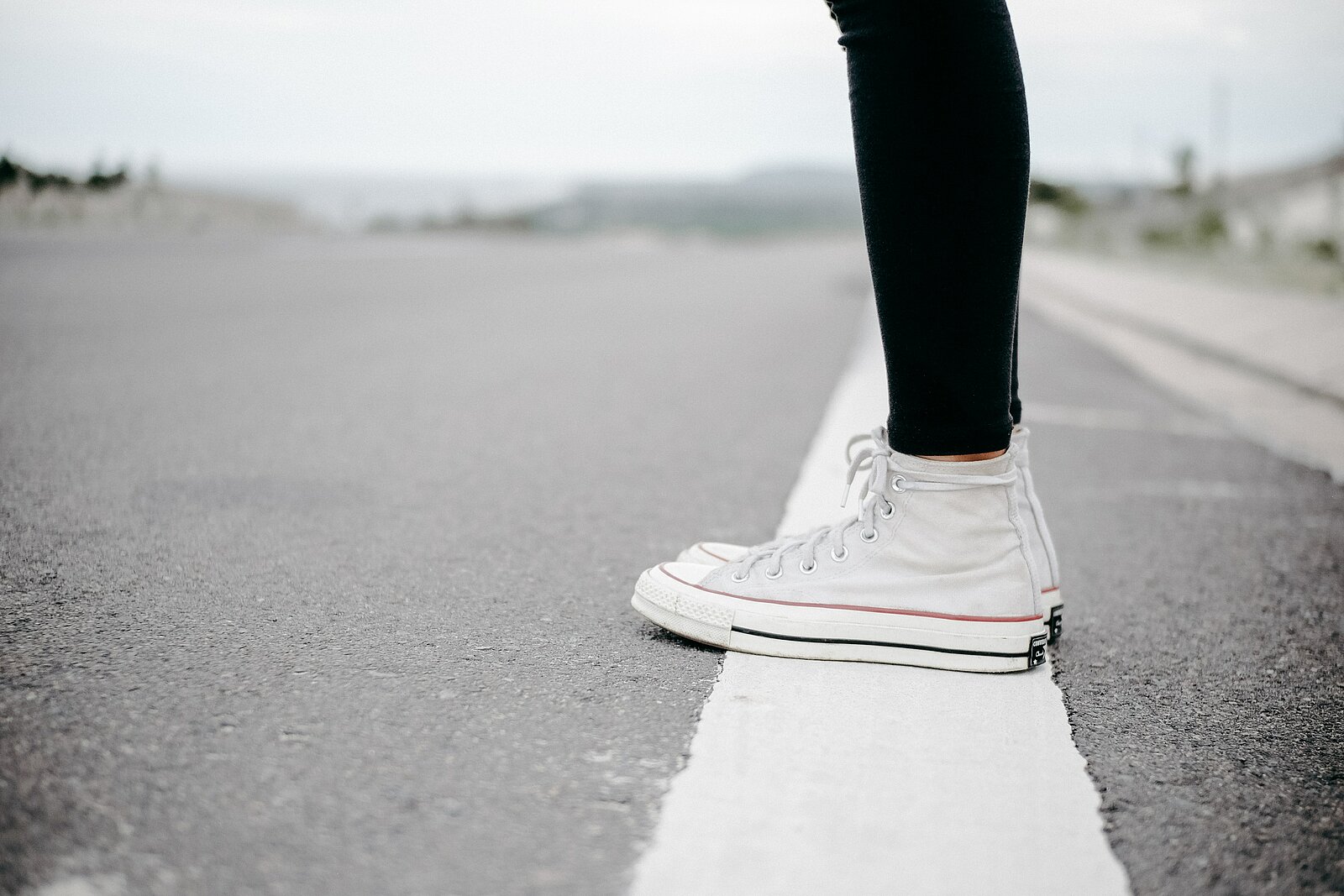 Weißer Sneaker auf einer Straßenmarkierung, im Hintergrund eine unscharfe Landschaft.