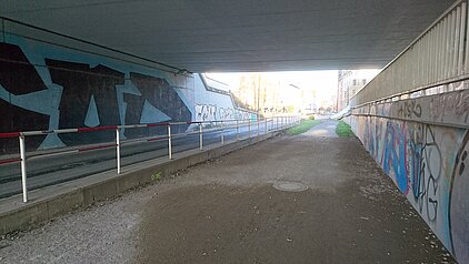 Unterführung mit Graffiti an den Wänden und einem Geländer entlang des Wegs