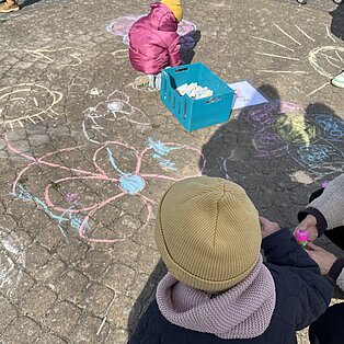 Kinder malen mit bunter Kreide Blumen und Sonne auf gepflasterten Boden