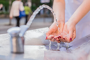 Frau hält Hände unter laufendem Wasser eines Trinkwasserbrunnens